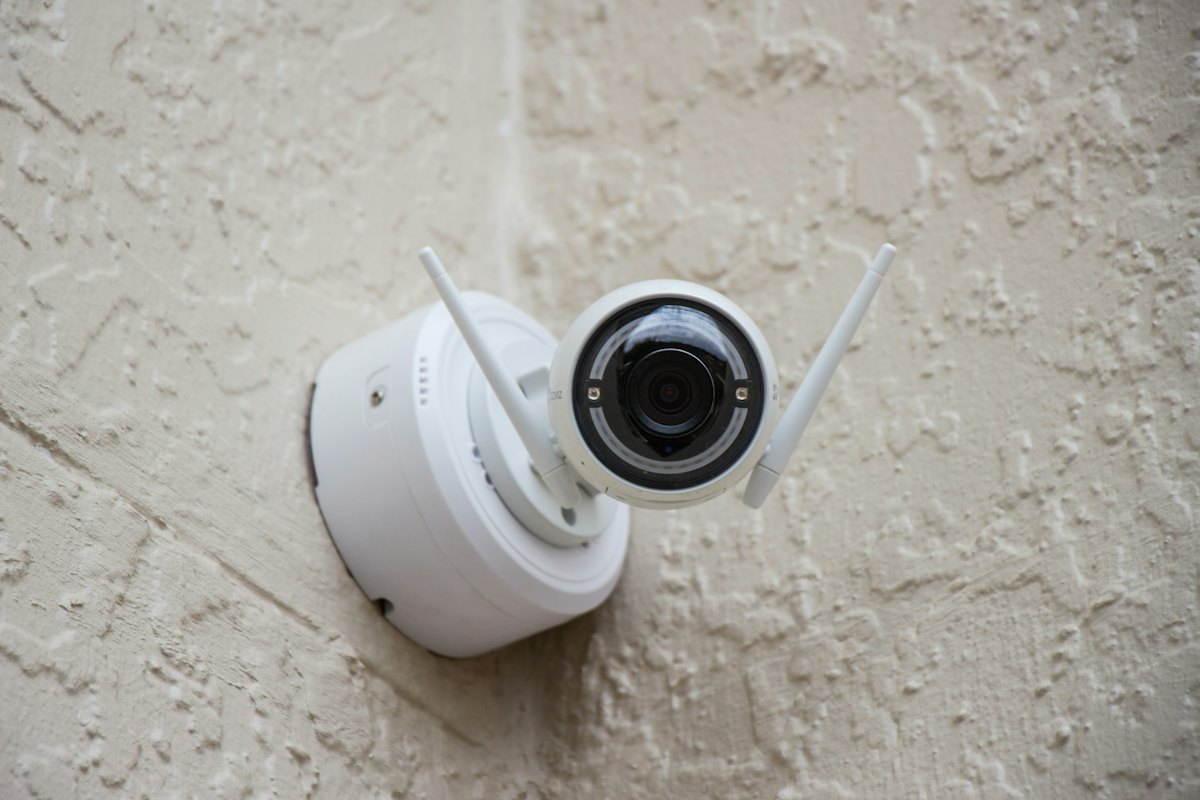 A small white security camera mounted on a wall.