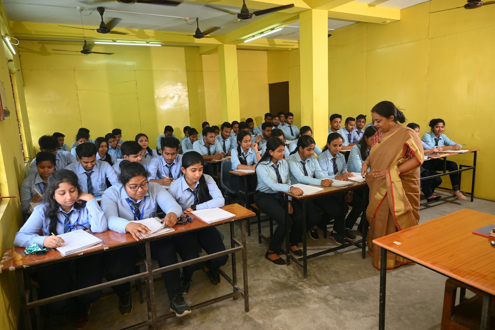 A teacher walking between rows of students in a classroom.