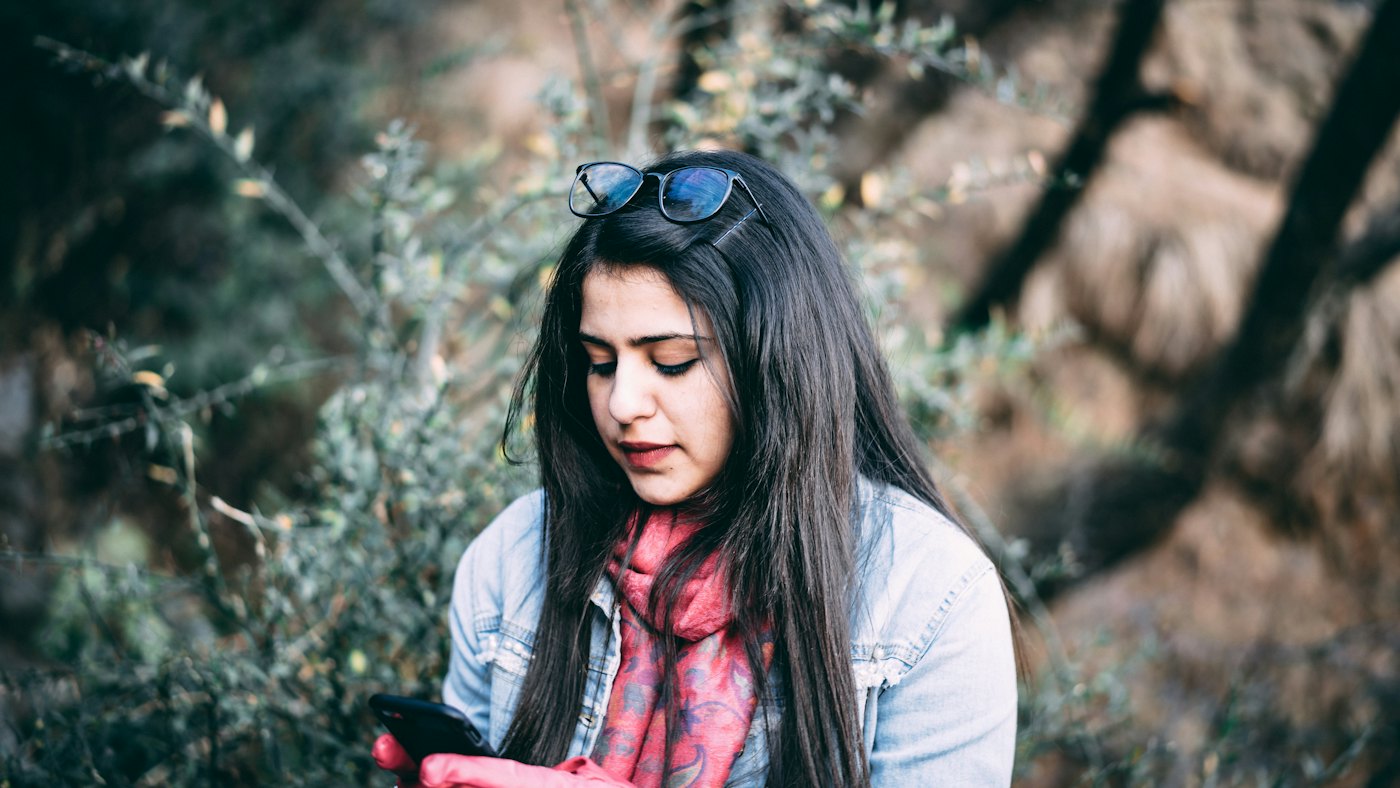 A young woman outdoors, looking at her phone.