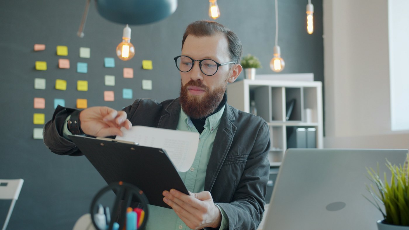 A man reviewing a document on a clipboard at his desk.