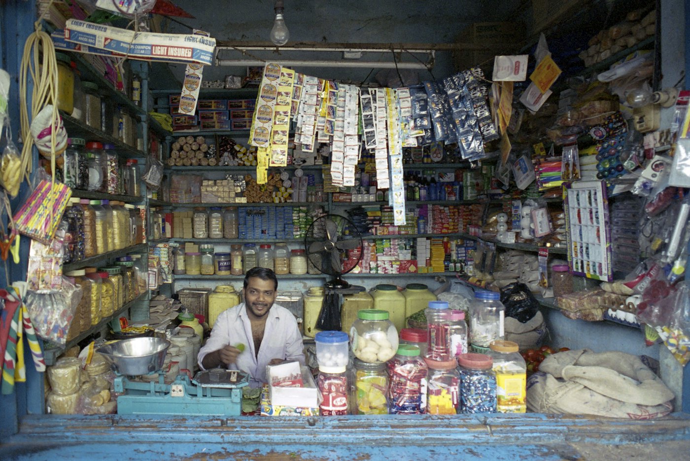 A shopkeeper smiling behind the counter of a packed general store.