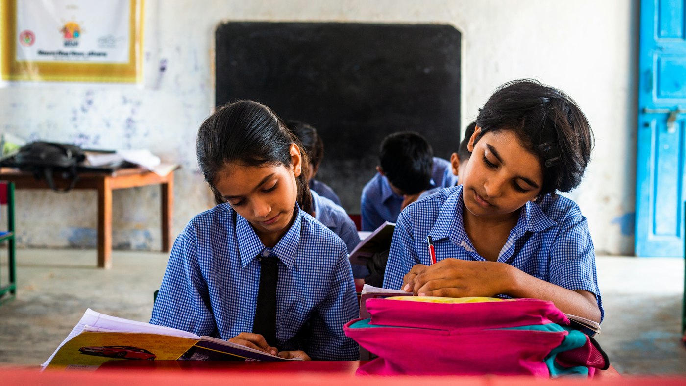 Two students in school uniform reading and writing at their desk.